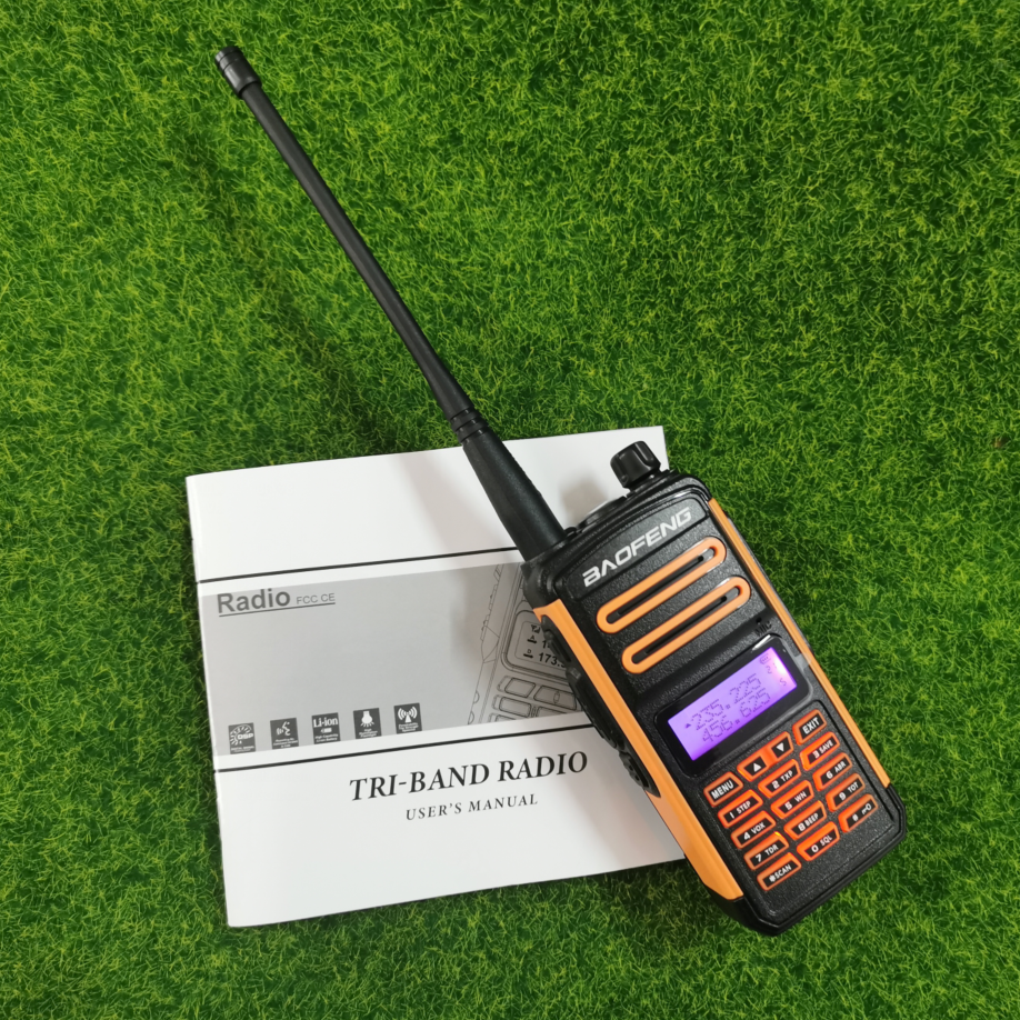 Baofeng TR-988UV triband radio with extendable antenna and user manual on grass backdrop