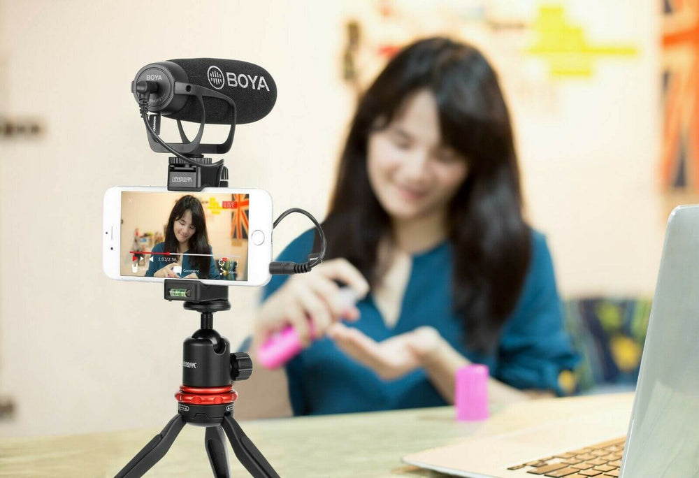 BOYA BM2021 shotgun microphone mounted on a tripod for smartphone video recording at a desk